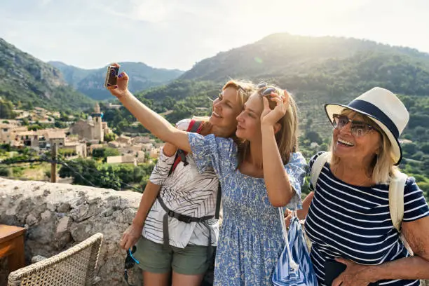 Multi generation family sightseeing beautiful town of Valldemossa. Sunny summer day in Majorca, Spain.
Teenage girl, mother and grandmother are taking selfies. Behind them there is a magnificent view of the town of Valldemossa and the surrounding mountains - Serra de Tramuntana.
Canon R5