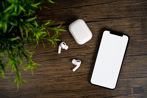 Smartphone with white on display, bluetooth headphones on wood table. Top view