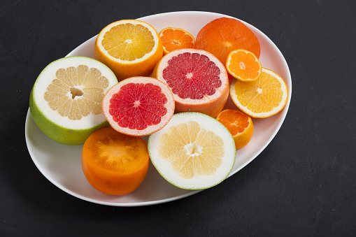 Fresh citrus fruits on white dish close up, dark background
