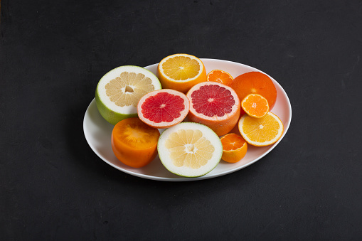 Fresh citrus fruits on white dish close up, dark background