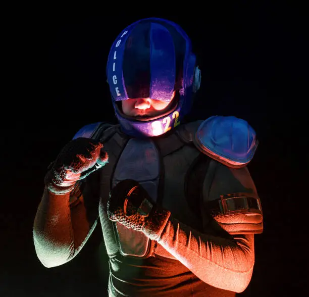 Male robot cop waves and punches his fits in dark. Halfman is ready for fight. Bionic cyborg looks at camera. Red blue light. Law and Order concept. World of tomorrow. Portrait