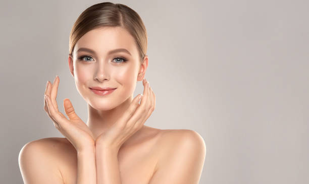 Gorgeous, young woman with clean, fresh skin is holding hands near the face. Light smile on the perfect face. Cosmetology. Symmetrical position of hands with graceful fingers in front young pretty face. Light smile on the perfect face. Facial treatment, cosmetology, beauty technologies and spa. semi dress stock pictures, royalty-free photos & images