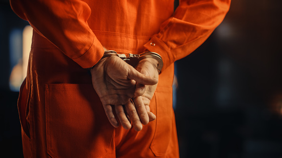 Cinematic Close Up Footage of a Handcuffed Convict at a Law and Justice Court Trial. Handcuffs on Accused Criminal in Orange Jail Jumpsuit. Law Offender Sentenced to Serve Jail Time.