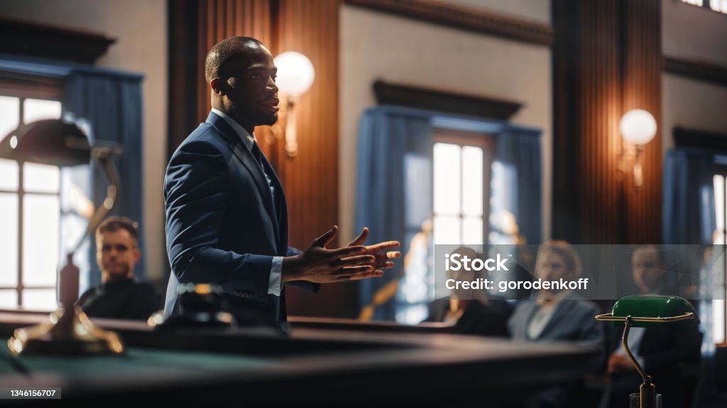 Court of Justice and Law Trial: Male Public Defender Presenting Case, Making Passionate Speech to Judge, Jury. African American Attorney Lawyer Protecting Client's Innocents with Supporting Argument. Lawyer Stock Photo
