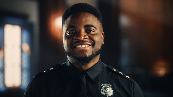 Retrato auténtico de un policía negro feliz y guapo con uniforme universal sonriendo a la cámara. Exitoso agente afroamericano de aplicación de la ley. Guardia de seguridad de la sala del tribunal en el trabajo. photo