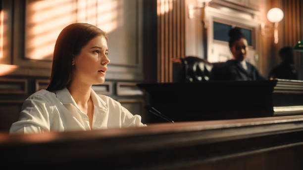 court of law and justice trial: portrait of beautiful female witness giving evidence to prosecutor and defence counsel, judge and jury listening. dramatic speech of empowered victim against crime. - domestic issues imagens e fotografias de stock