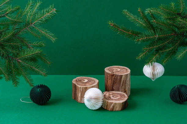 istock Three empty wooden podiums with rough textured surface, white paper Christmas decorations and fir tree branches on green background. Trendy natural cosmetic product presentation mockup. Still life 1346157978