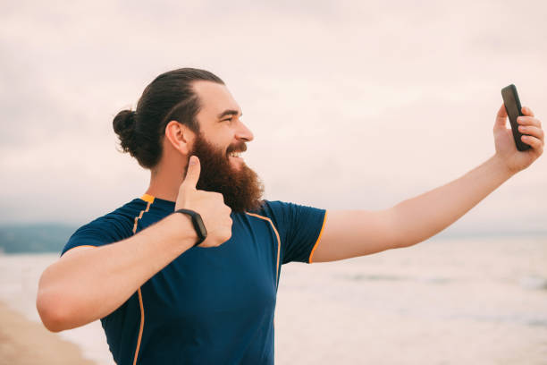 Bearded hipster man is taking a selfie after running on the beach. stock photo