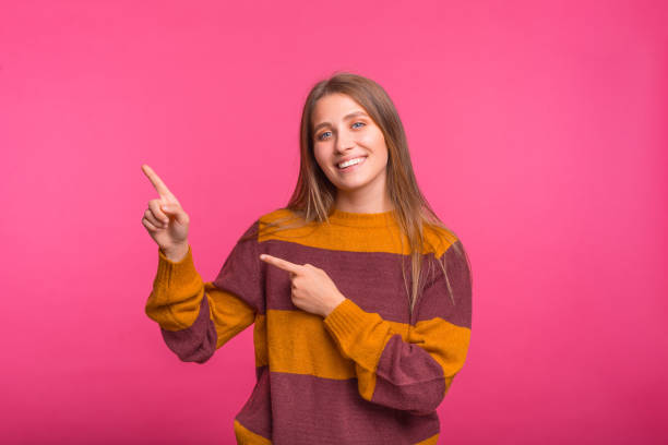 istock Smiling girl is pointing with both hands on the pink background. 1346168006