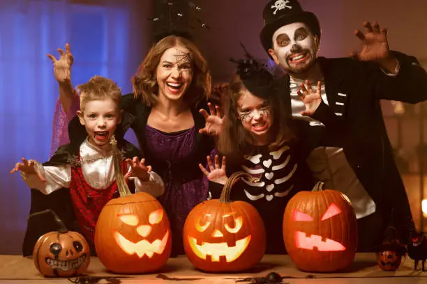 Photo of Young family mother father and children in Halloween costumes celebrating all hallows eve at home