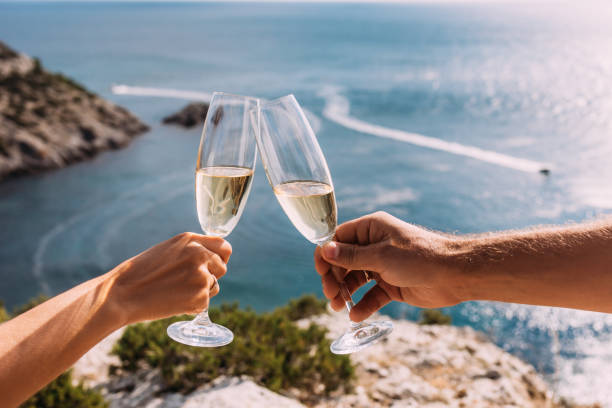 Hands holding champagne glasses over the sea. Romantic vacation. Two hands holding champagne glasses on the background of the sea. A couple in love drinks champagne on the seashore. Copy space stock photo