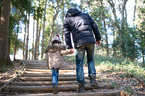 Father and daughter walk in the woods holding hands
