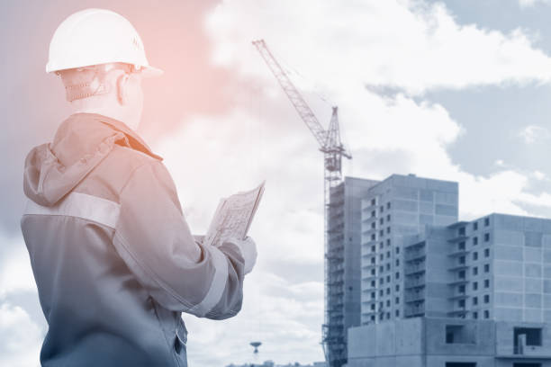 istock An engineer, architect, builder holds in his hands a plan of new buildings on the background of construction. Double exposure, collage. Selective focus. Tinted image. 1346172565