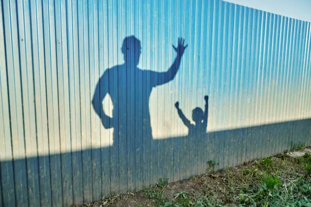 Photo of Shadows of father and little kid on metal fence at sunset