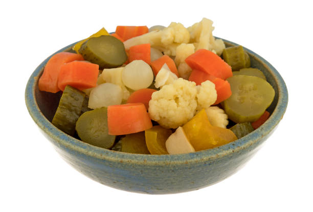 Side view of giardiniera pickled vegetables in a stoneware bowl isolated on a white background.