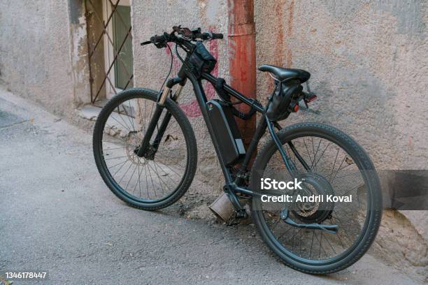 Black Electric Bicycle With Battery On The Frame Stands On The Citys Street Near The Wall Outdoor Transportation Electricity Electric Ecological Electric Drive Engine Stock Photo - Download Image Now