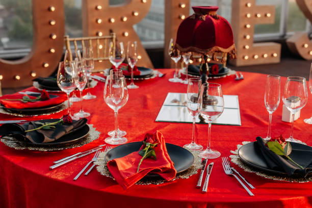 istock Guests table setting for banquet in black, red and gold style. Elegant dinner: decor, tablecloth, plates with napkins and fresh roses, glasses, cutlery. Themed party celebration on the roof, outdoor. 1346181393