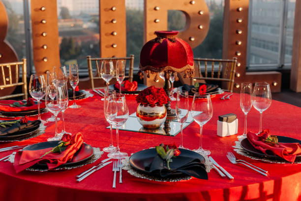 istock Guests table setting for banquet in black, red and gold style. Elegant dinner: decor, tablecloth, plates with napkins and fresh roses, glasses, cutlery. Themed party celebration on the roof, outdoor. 1346181471