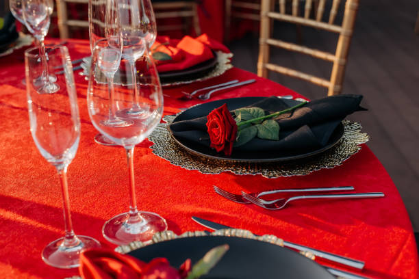 istock Guest table setting for banquet in black, red and gold style. Elegant and luxury dinner arrangement: decor, tablecloth, plates with napkins and fresh roses, glasses, cutlery. Themed party celebration 1346181525