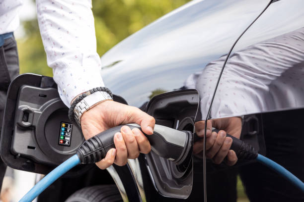 Human hand is holding charging connect power supply plugged into an electric car stock photo