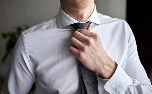 man in shirt dressing up and adjusting tie on neck at home