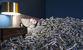 Smiling man sleeping in a bed covered with dollars