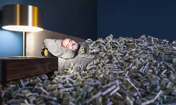 Smiling man sleeping in a bed covered with dollars money. wealth concept.