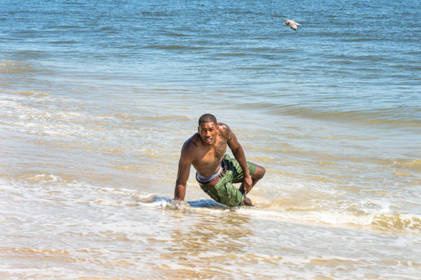 istock Young black man, shirtless, playing with water on beach 1346182836