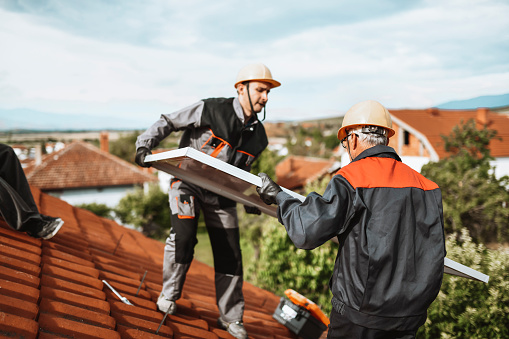 Workers On Rooftop Positioning And Installing Solar Panel