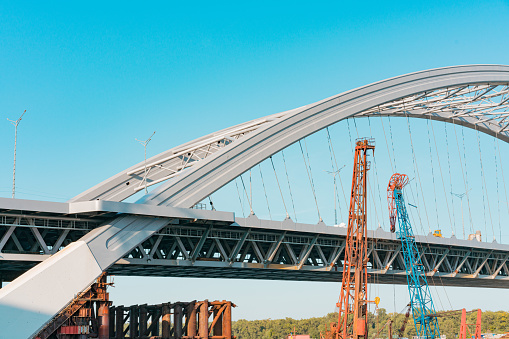 Arch brand new bridge with temporary metal supports and cranes which dismantling them. Construction. Steel. Industrial