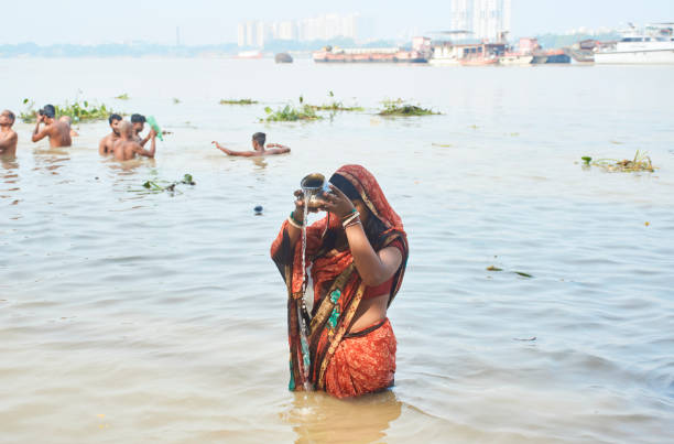 Performing religious customs on holy Ganges river Babughat, Kolkata, 10/12/2021: A Hindu woman offering prayer to Sun God while bathing in holy Ganges water. It is an age old tradition still followed by large number of Indians. waist deep in water stock pictures, royalty-free photos & images