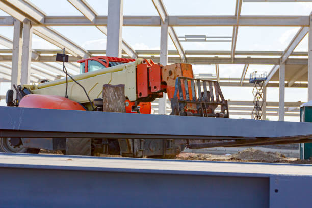 Telescopic forklift that until he transporting pile of painted, welded metal beams, structure girders for metal construction at building site.
