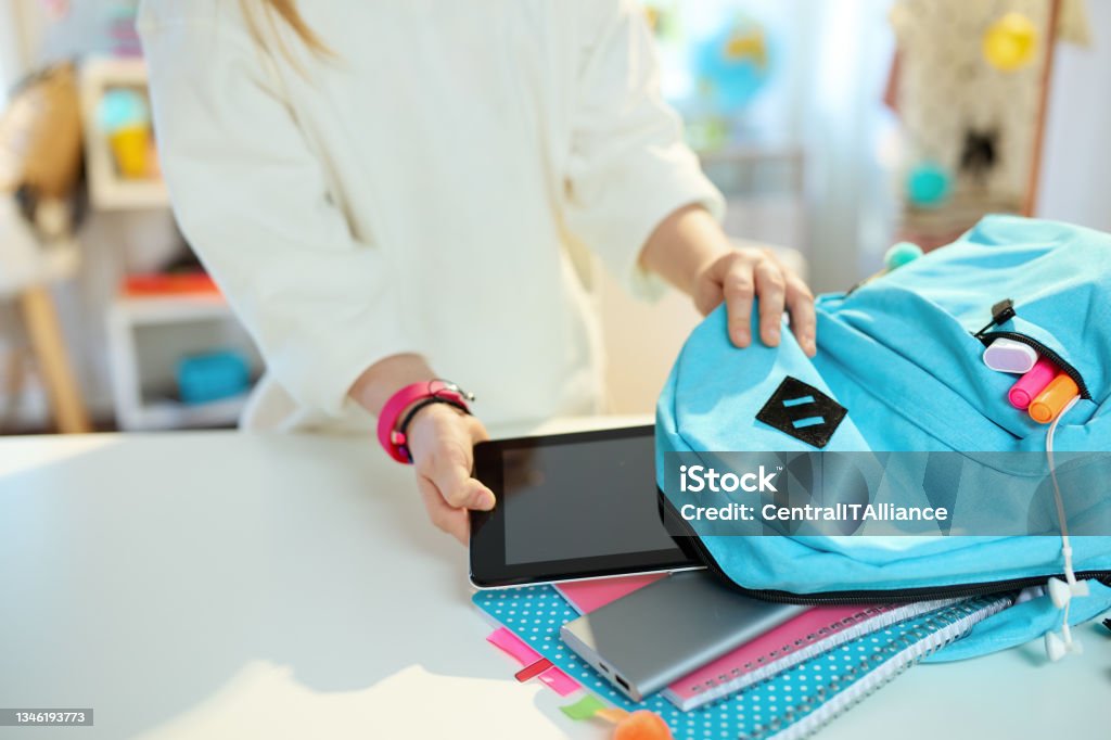 Modern school girl packing for school at home in sunny day Closeup on school girl with tablet PC, workbooks and blue backpack packing for school at home in sunny day. Backpack Stock Photo