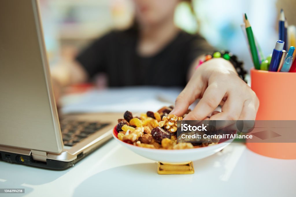Modern school girl distance learning and eating healthy snack Closeup on school girl with laptop distance learning and eating healthy snack at home in sunny day. Snack Stock Photo