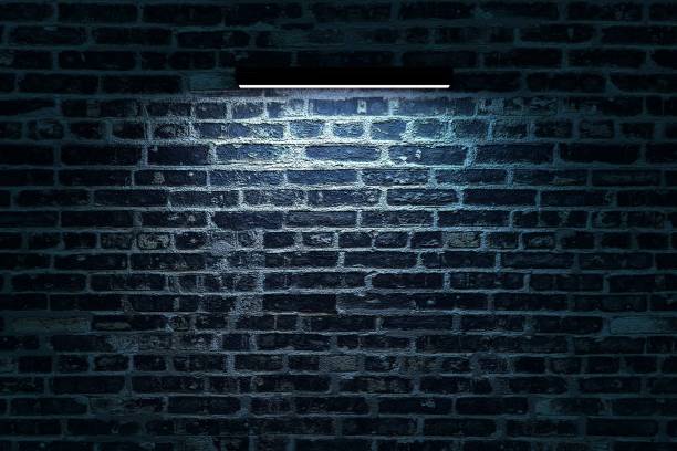 istock Long wall lamp illuminates a brick wall. Neon lamp is hanging on a brick wall. Dark isolated background. 3D graphics. Interior design 1346196424