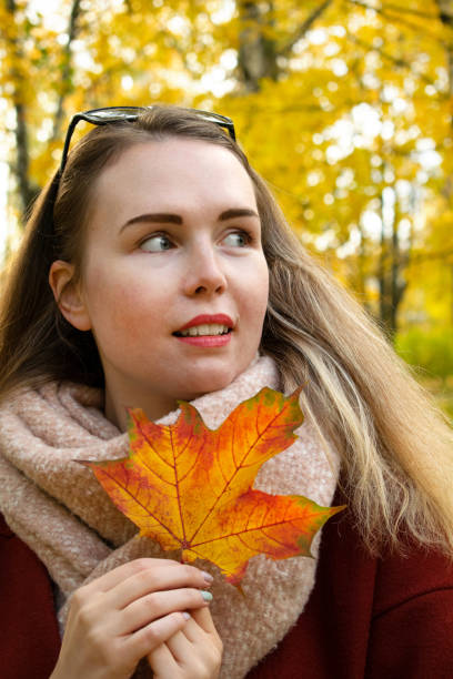 istock Young woman wearing warm scarf is holding maple leaf 1346197654