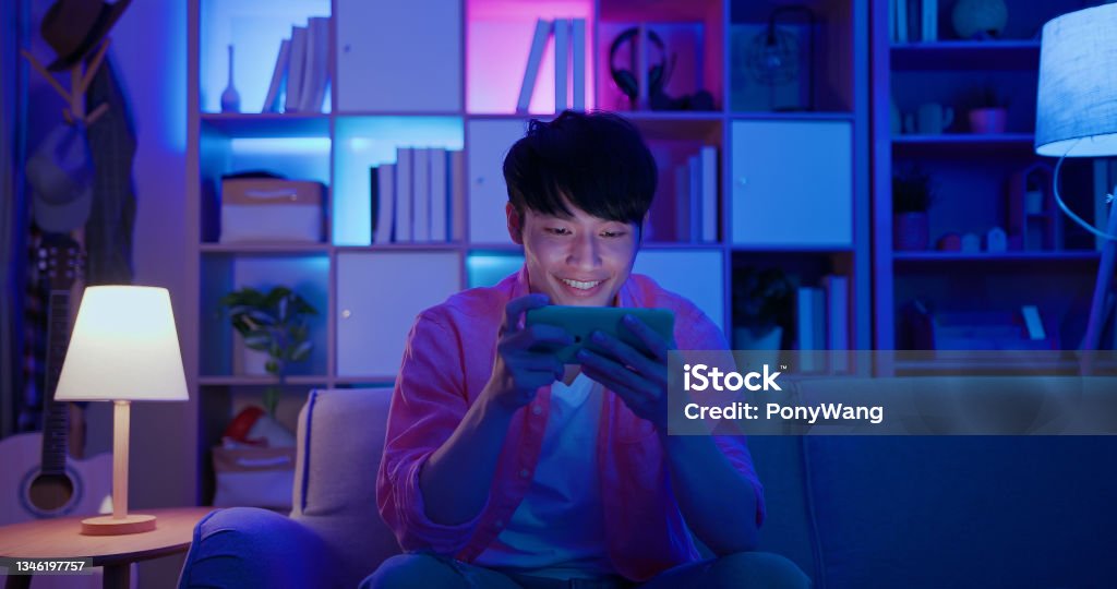 man plays mobile games asian man plays mobile games on sofa in the evening at home Video Game Stock Photo