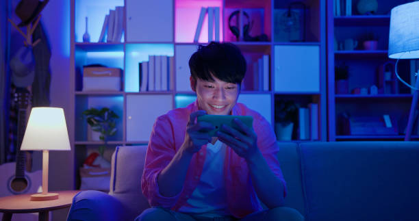 man plays mobile games asian man plays mobile games on sofa in the evening at home gamer stock pictures, royalty-free photos & images