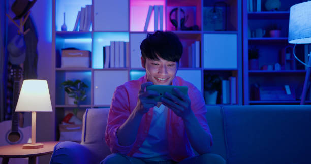 man plays mobile games asian man plays mobile games on sofa in the evening at home games console stock pictures, royalty-free photos & images