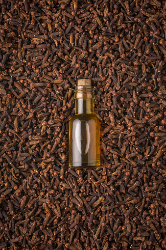 glass bottle of clove oil with dry cloves, aromatic spice and herb with essential oil, top view