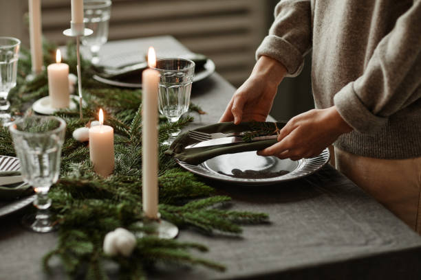Setting Elegant Christmas Table Side view close up of unrecognizable woman setting up dining table decorated for Christmas with fir branches and candles in grey tones, copy space christmas decore candle stock pictures, royalty-free photos & images