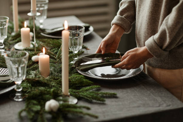 Setting Elegant Christmas Table Side view close up of unrecognizable woman setting up dining table decorated for Christmas with fir branches and candles in grey tones, copy space dining table stock pictures, royalty-free photos & images