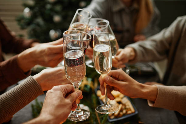 Toasting at Christmas Dinner Close up of friends clinking champagne glasses while enjoying Christmas dinner together sitting by elegant dining table with candles people banque stock pictures, royalty-free photos & images