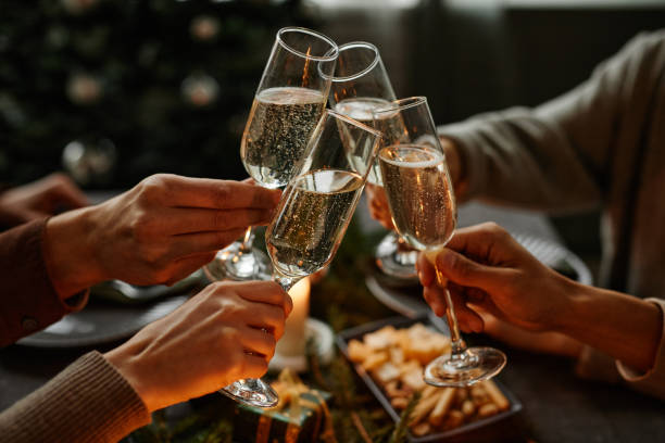 Toasting with Champagne at Christmas Dinner Close up of four people enjoying Christmas dinner together and toasting with champagne glasses while sitting by elegant dining table with candles champagne stock pictures, royalty-free photos & images