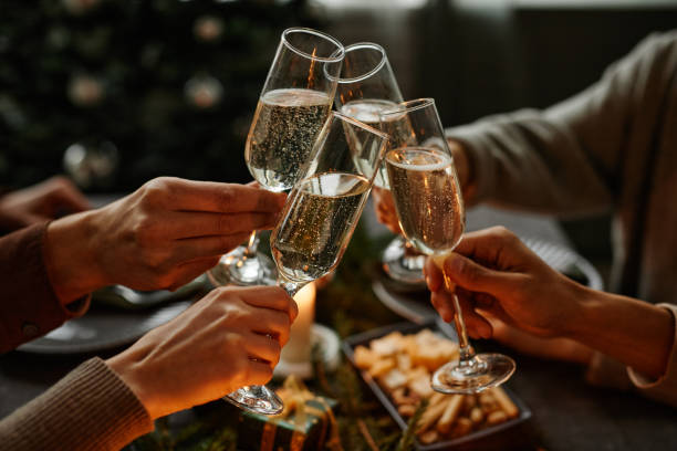 Toasting with Champagne at Christmas Dinner Close up of four people enjoying Christmas dinner together and toasting with champagne glasses while sitting by elegant dining table with candles honour stock pictures, royalty-free photos & images