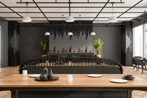 View of the classy grey and black cafe interior, having a neat sofa headboard with a wooden tabletop on the forefront. Parquet. A concept of modern restaurant design. 3d rendering