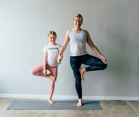 Mom and daughter in yoga balance pose in the gym.