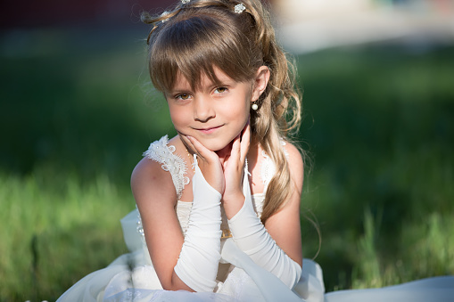 Portrait of a beautiful girl of six seven years in a white dress on the grass.