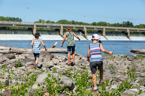Rear view of three children walking on the riverbank of the Mississippi River near the Coon Rapids Dam in Minnesota, USA. Taken on a beautiful summer day.