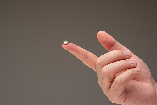 Very small button L1131 battery cell set on Caucasian male's index finger. Close up shot, isolated on gray background.